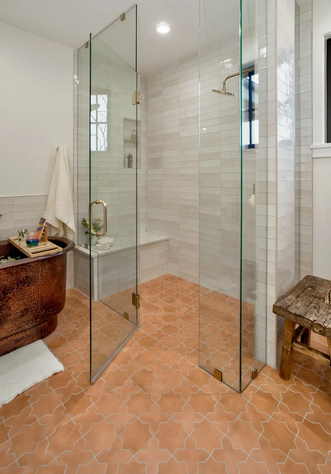 Modern bathroom featuring geometric terracotta floor tiles, a glass-enclosed shower, and a copper bathtub.